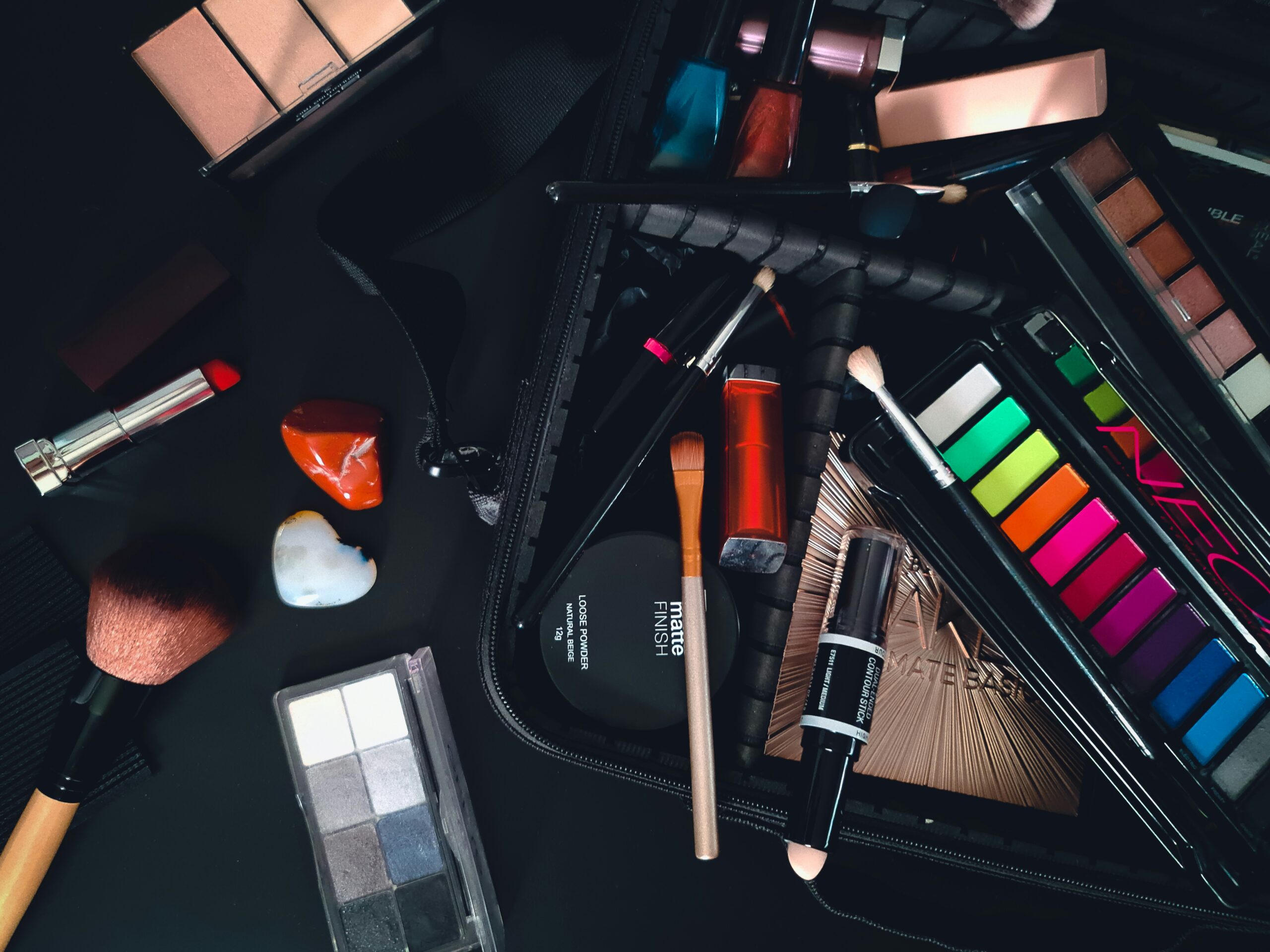 Dark photo. Black background. Makeup brushes, eye shadow pallets and foundation strewn about