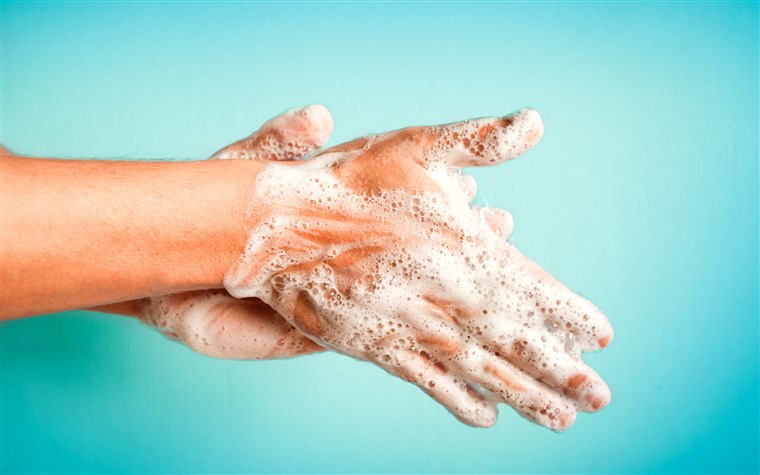 White or beige hands covered in soap in front of a light blue background