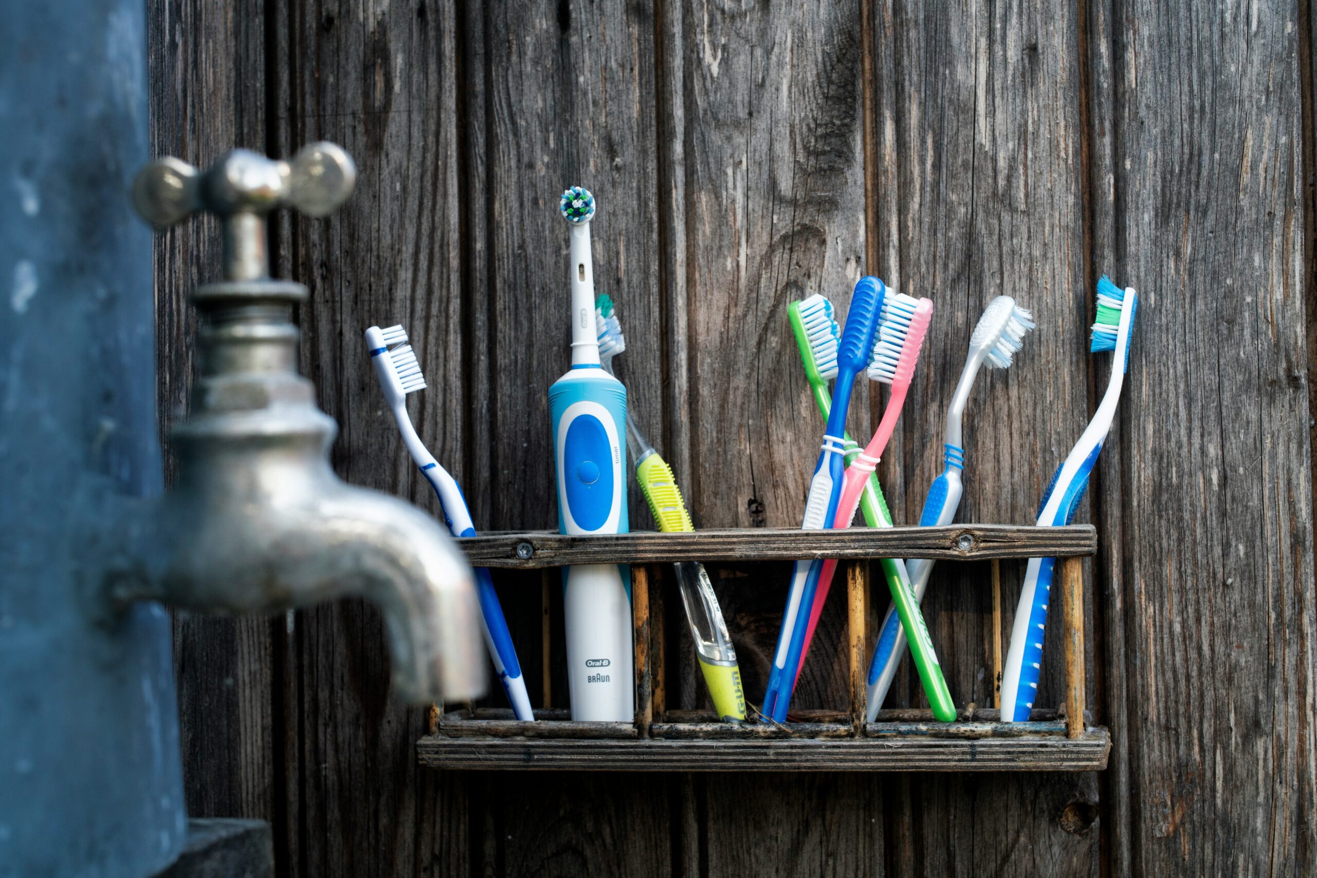 Plastic toothbrushes of various colors and an electric toothbrush sitting on a wooden shelf