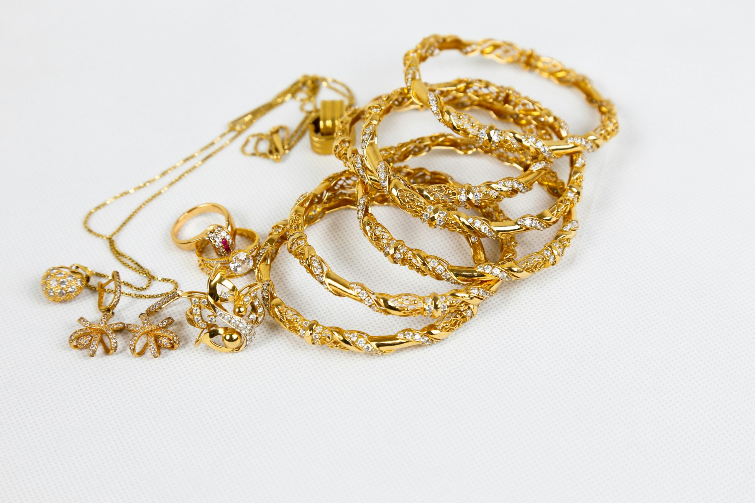 An assortment of gold necklaces, rings, earrings and bangles in a pile on a white background