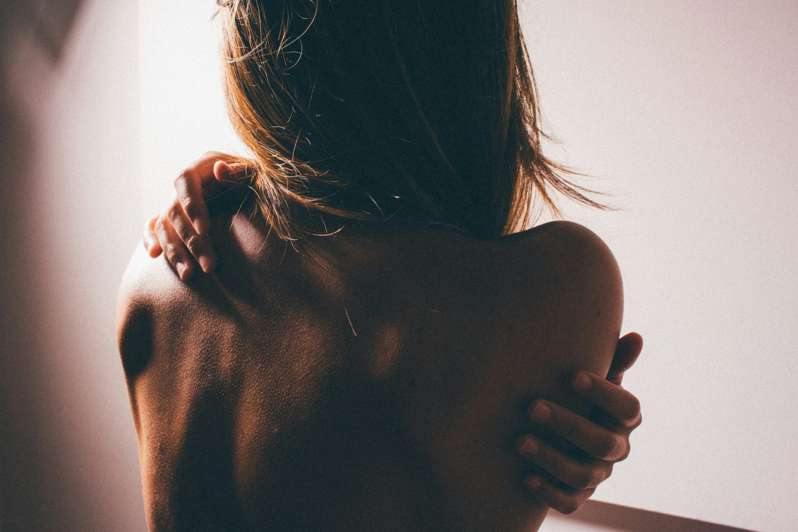 Photo of back of woman who is hugging herself. Dark setting, very shadowed.