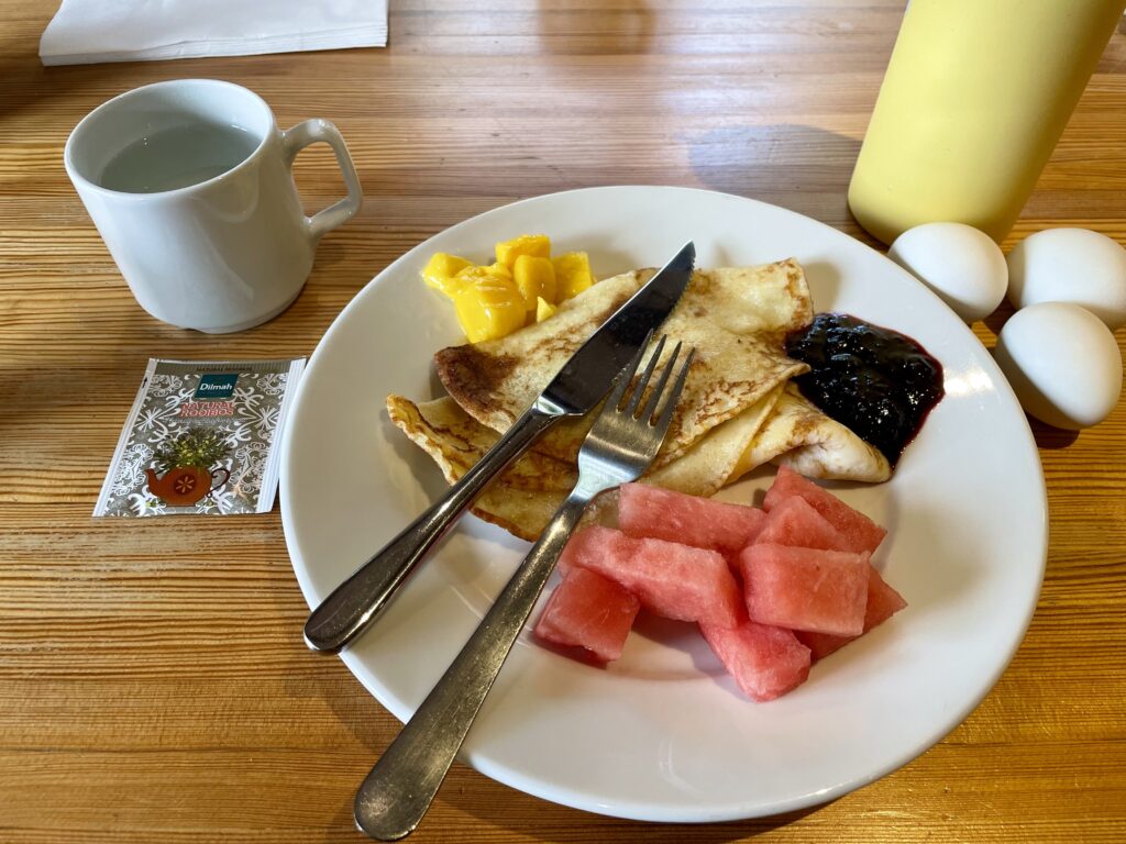 Photo of a plate of crepes and fresh fruit, a cup of tea and three hardboiled eggs.