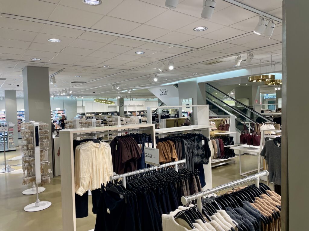 Photo of a department store with clothes on racks. All the clothes are white, black, brown, gray.