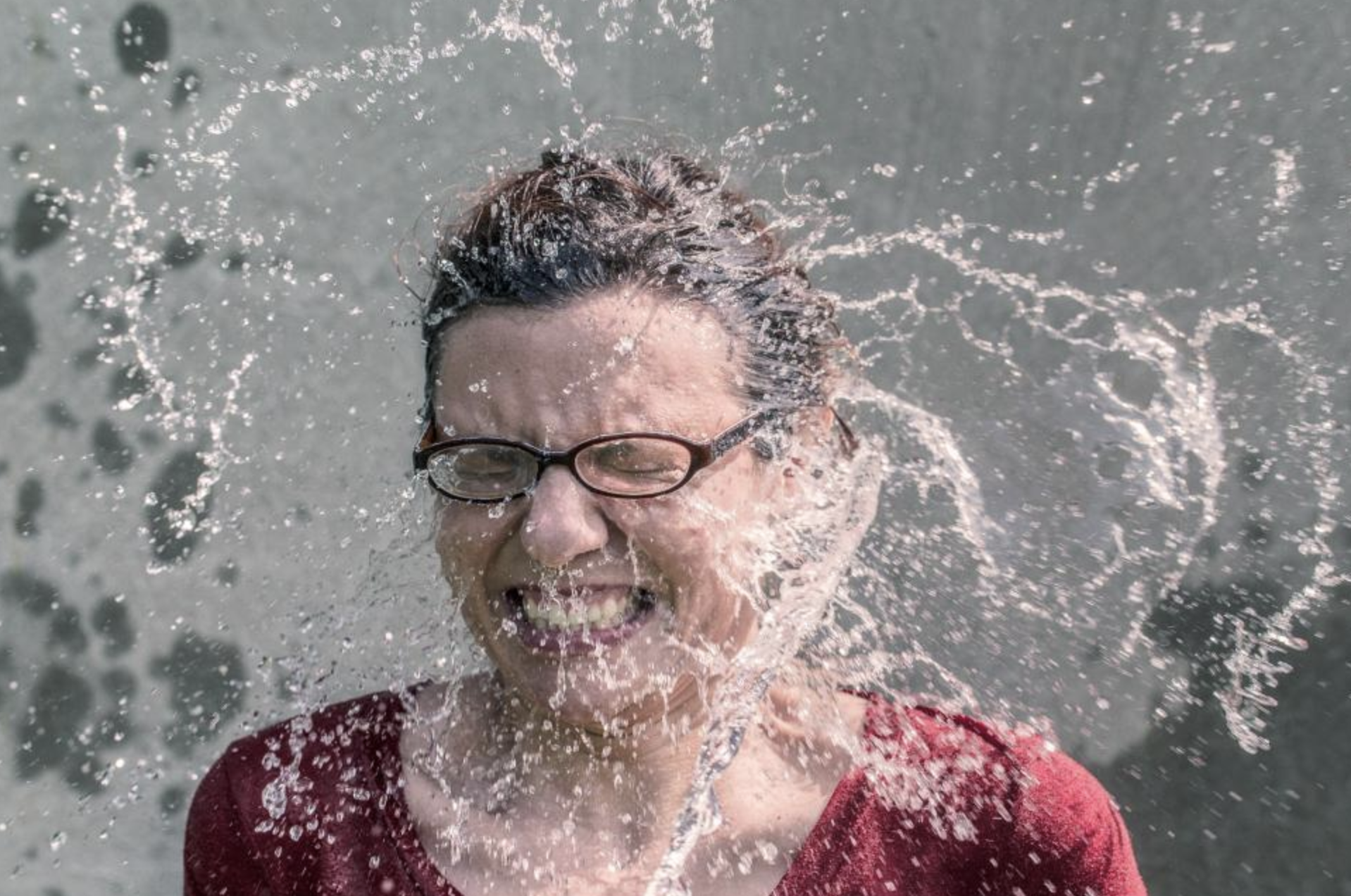 woman wearing glasses getting splashed in the face with water