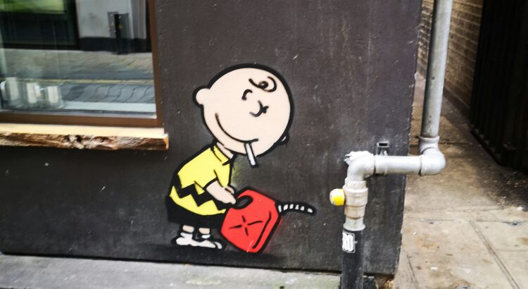 Graffiti depicting Charlie Brown holding a cigarette and a gas can on the side of a brown building.